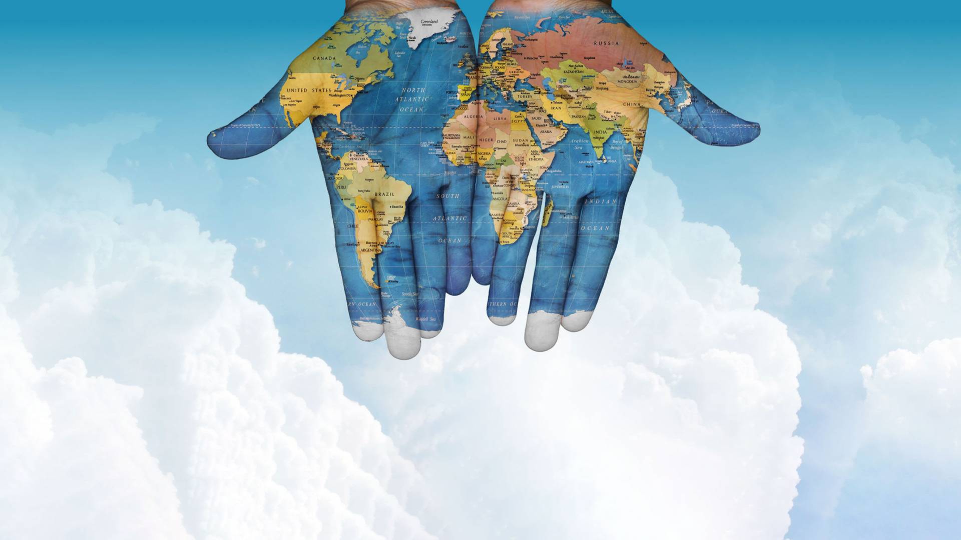 open hands painted with a map of the world with puffy clouds and blue sky in the background