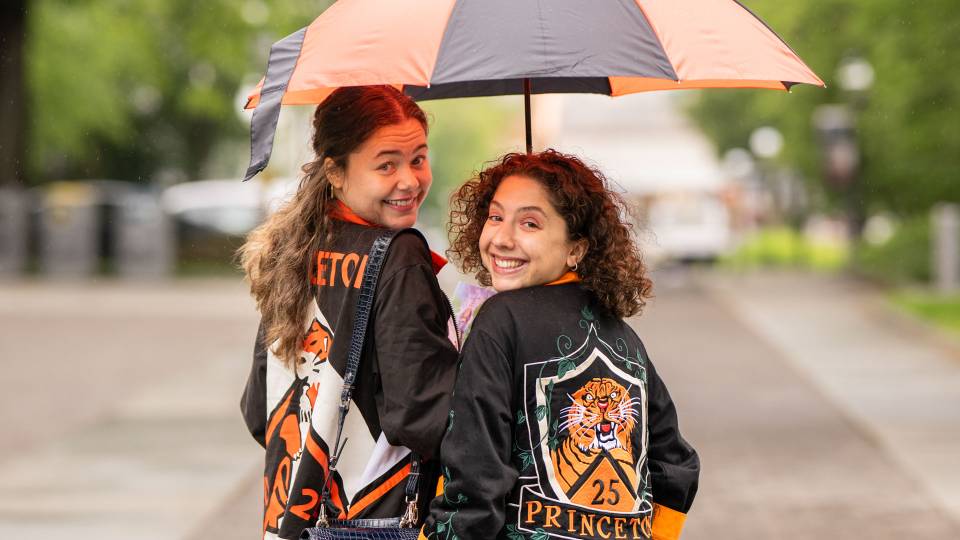 Two alumni smile under an umbrella 