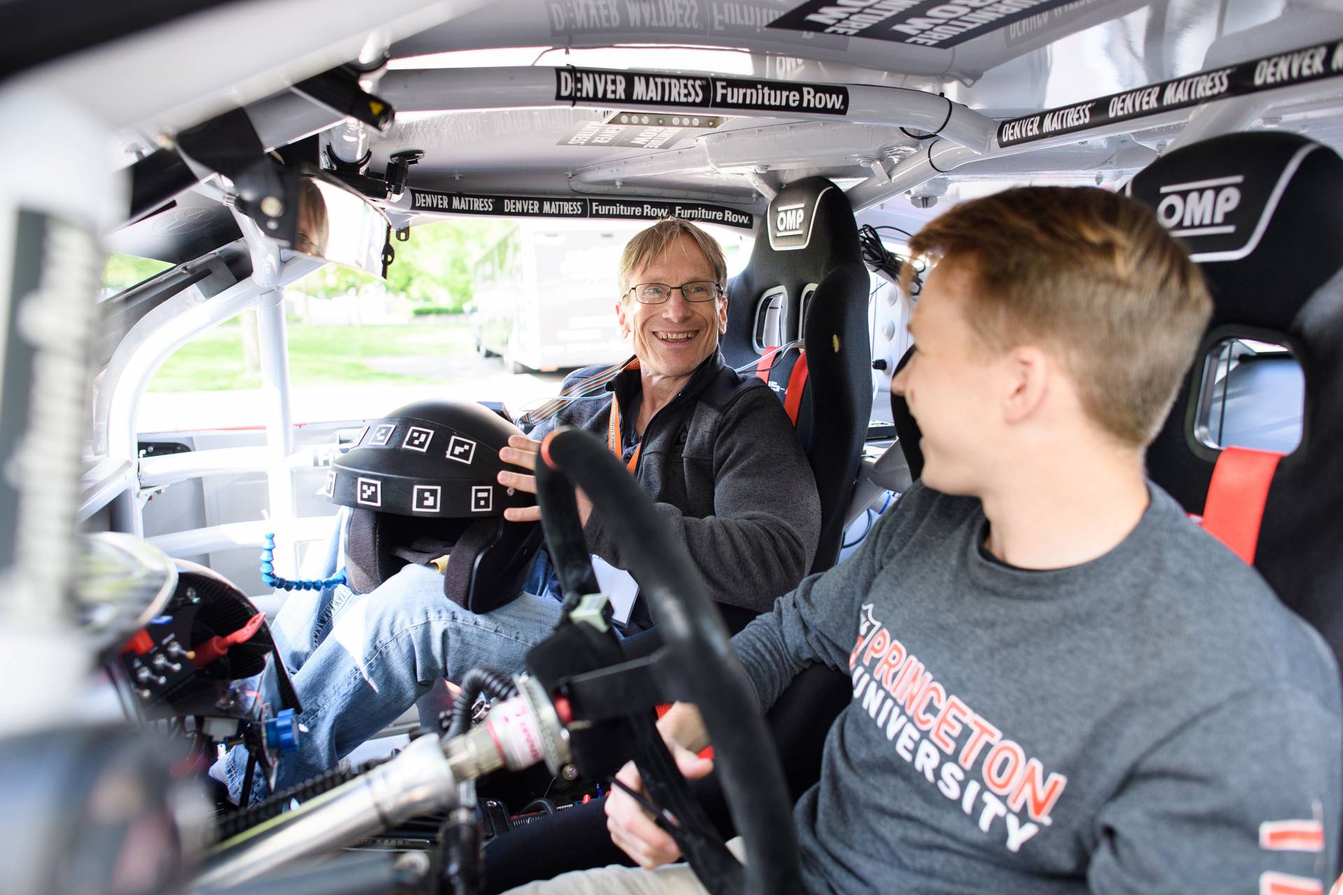 Two men sit in a smart NASCAR